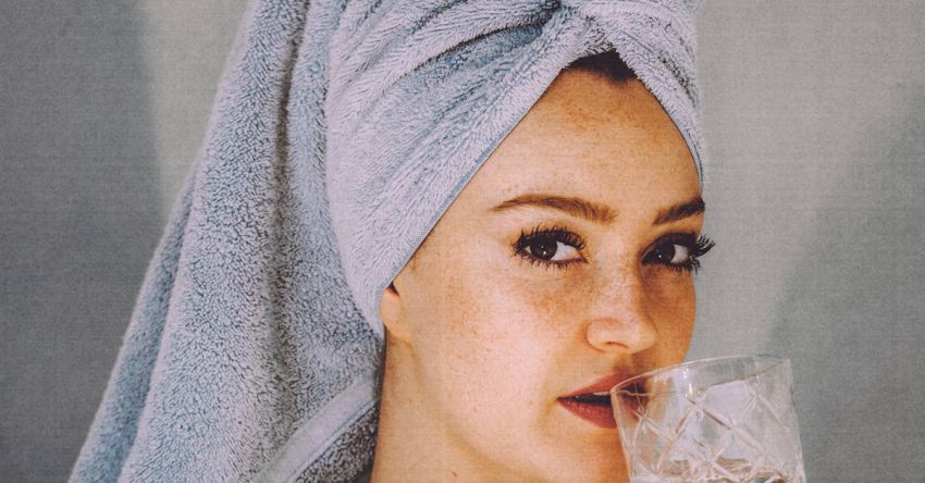 Pleasures - Young woman with hair wrapped with towel and bared shoulders drinking water and looking at camera